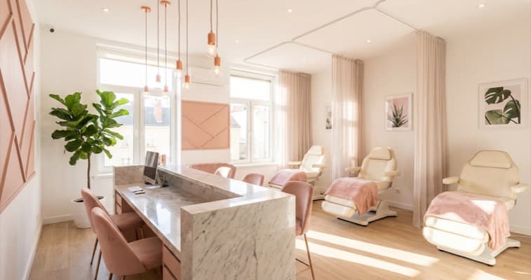 A bright contemporary beauty salon interior with a stylish reception desk, pendant lighting, and blush pink accents