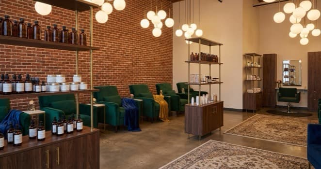 A luxury beauty salon interior with velvet treatment chairs, warm pendant lighting, and elegant shelving displaying beauty products