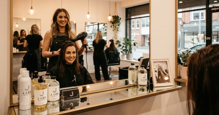 A confident hairdresser at their personalised styling station in a busy salon with business cards and personal product line visible