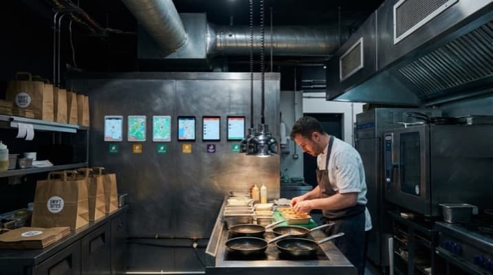 Busy dark kitchen with chefs preparing delivery orders across multiple stations