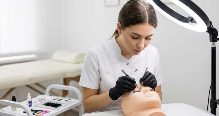 Lash technician in training practising extension application on a mannequin head