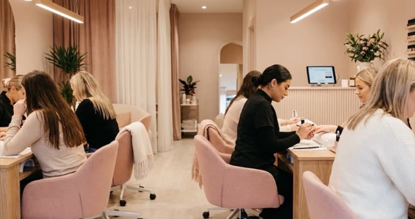 A busy modern nail bar with manicure stations, warm lighting, and clients being served
