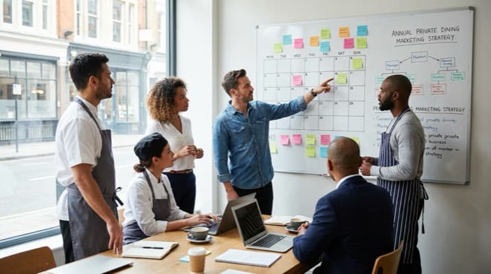 Restaurant manager reviewing a private dining marketing strategy calendar on a whiteboard