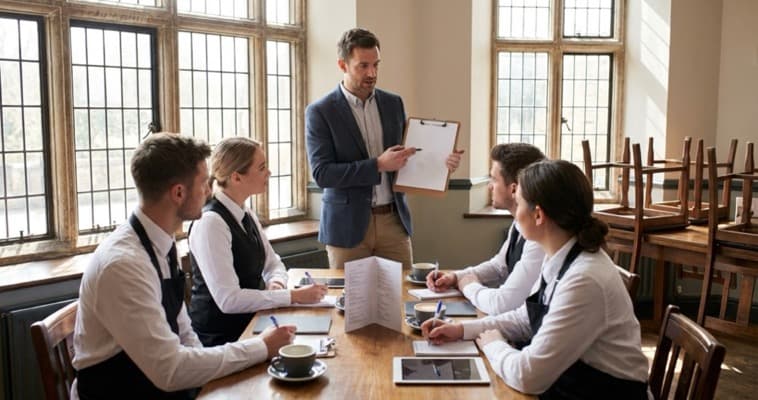 Restaurant manager leading a pre-shift upselling training briefing with front-of-house staff