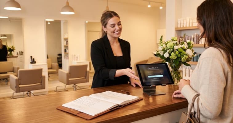 A salon reception showing a tablet with digital check-in screen next to a traditional appointment book