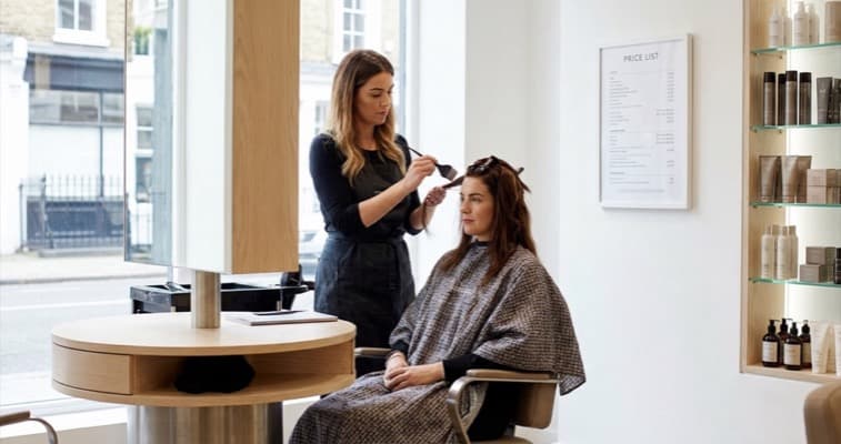 Hairdresser applying colour treatment to client in a modern UK hair salon with price list on wall